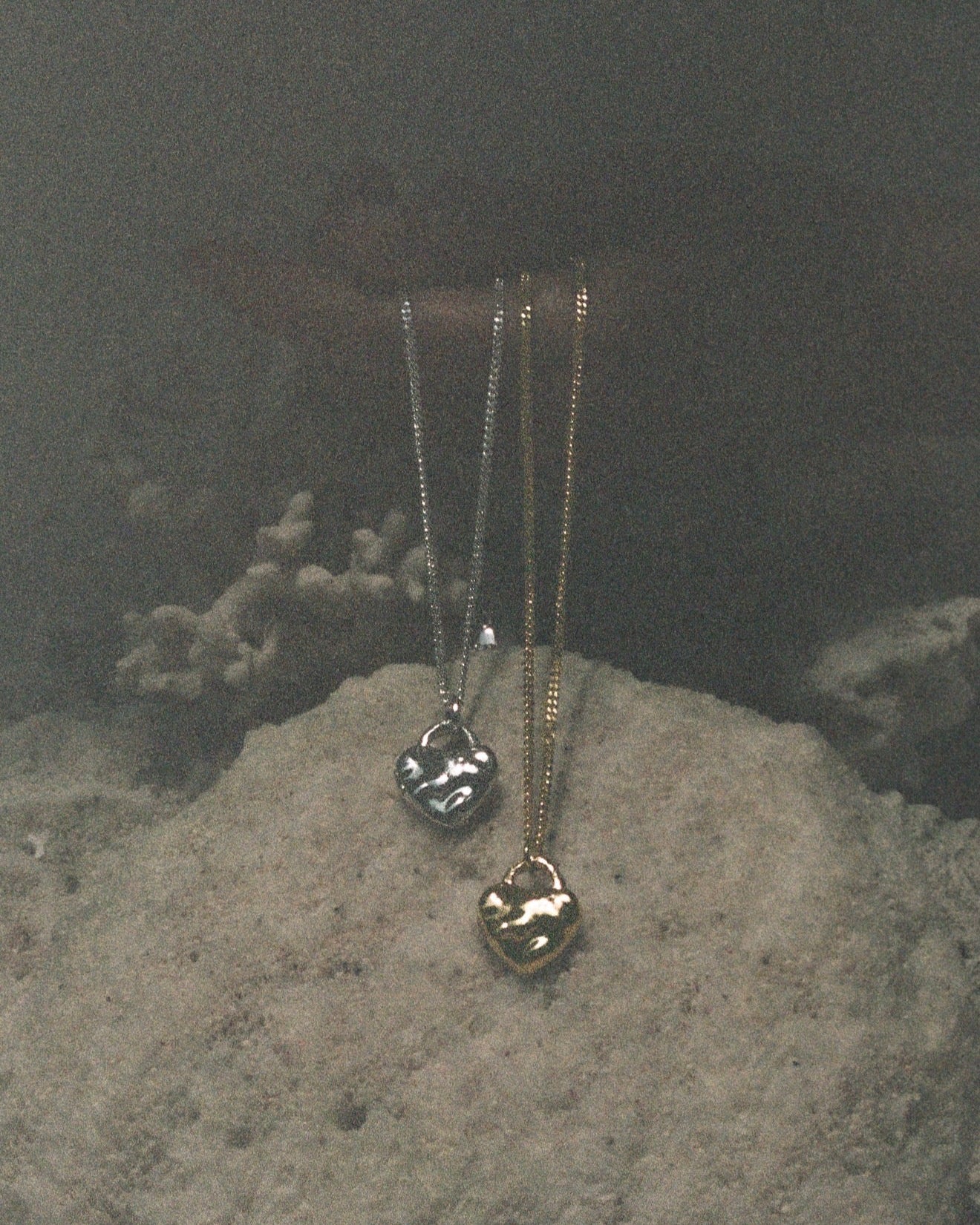 Two gold necklaces with heart pendants on a textured stone surface.