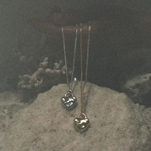 Two gold necklaces with heart pendants on a textured stone surface.